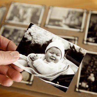 Mature person's hand holding sepia toned 1950s style photograph of young baby in pram